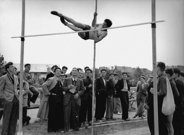 1946-1947. Championnat de l'Orne ASSU. P. Mazeaud saute à la perche (en tirant la langue), sous le regard attentif du juge M. Musot,...